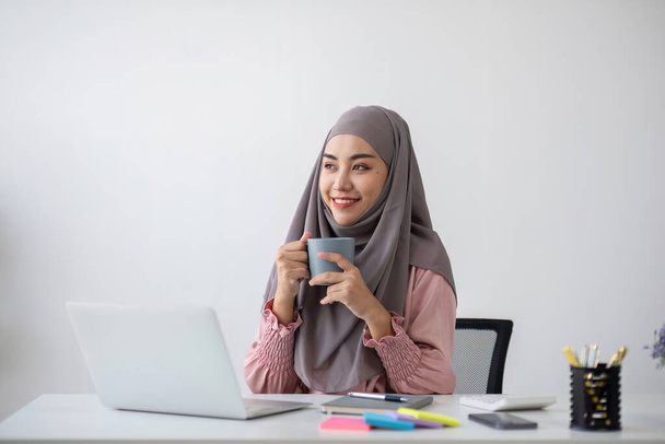 Smiling Muslim business woman Wearing a hijab while chatting online on a work desk in the office.. - Photo, Image
