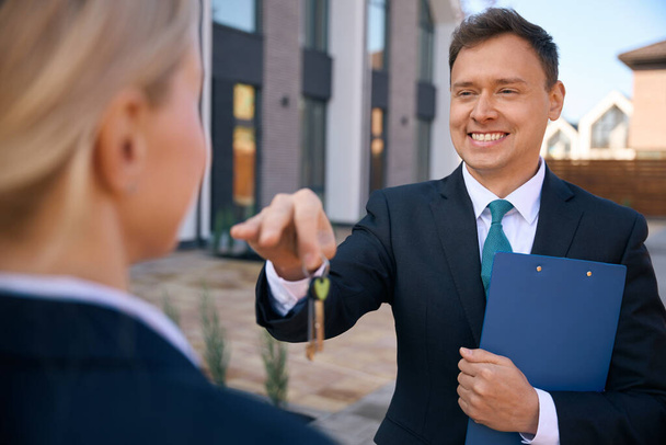 Обрізана фотографія щасливого чоловіка брокера з нерухомості дає ключі леді, в той час як обидва вони стоять поруч з будинком - Фото, зображення