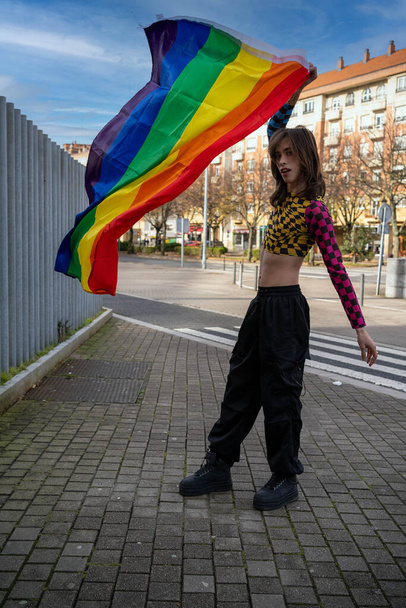 jongeman gekleed in kleurrijke en strakke kleding zwaaiend met de trots vlag in de wind.pride dag concept - Foto, afbeelding