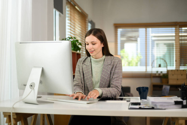 Mulher empresária caucasiana sorridente trabalhando em um computador em seu escritório em casa. - Foto, Imagem