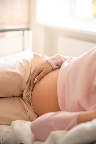 Onherkenbare vrouwelijke patiënt ligt op bed in ziekenhuisafdeling voor de bevalling - Foto, afbeelding