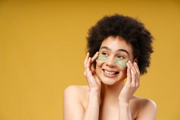 Mulher afro-americana atraente e sorridente com cabelos encaracolados com manchas oculares olhando para a câmera, posando isolada no espaço de cópia de fundo amarelo. Conceito de cuidados com a pele, dermatologia - Foto, Imagem