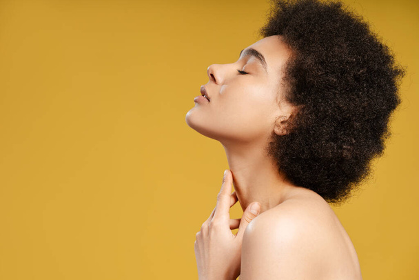 Sexy, bella donna afroamericana che si tocca il collo, con gli occhi chiusi in posa isolata su sfondo giallo, spazio copia. concetto di pubblicità, cosmetologia - Foto, immagini
