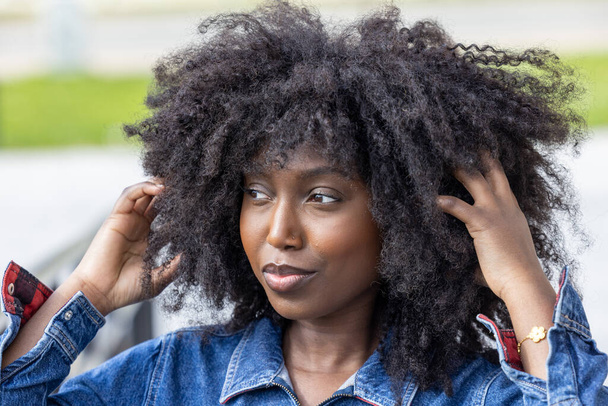Eine Nahaufnahme zeigt eine elegante Afroamerikanerin im Jeans-Outfit, deren natürliches Haar ihr Gesicht umrahmt. Ihr seitlicher Blick und das subtile Lichtspiel ihrer Gesichtszüge schaffen ein fesselndes Porträt - Foto, Bild