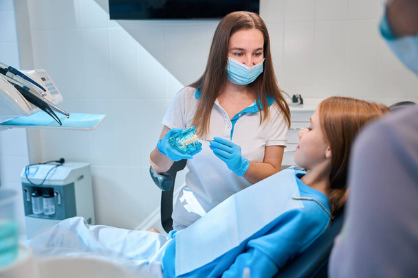 Κορίτσι που συμβουλεύεται οδοντίατρο σε σύγχρονη κλινική, γυναίκα που εργάζεται με βοηθό - Φωτογραφία, εικόνα