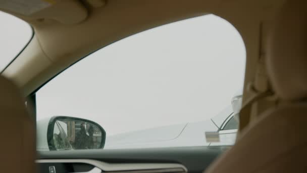 Un ladrón de coches mira a través de la ventana del coche, sosteniendo una llave para romper el vidrio. una escena de vandalismo y robo de auto inminente - Imágenes, Vídeo