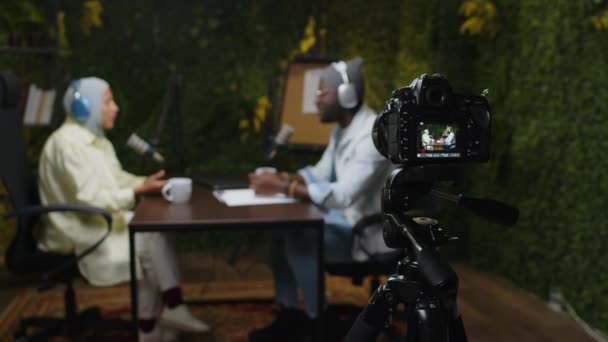 Ψηφιακή κάμερα σε τρίποδο κινηματογραφώντας βίντεο μαύρων blogger και γυναικών με χιτζάμπ που ηχογραφούν podcast στο στούντιο. Εστίαση σε νέα στοιχεία - Πλάνα, βίντεο