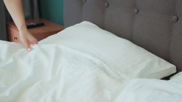 In de slaapkamer persoon verzorgt bed opmaken om minutieus in te stoppen lakens pluis kussens. Met elke precieze beweging maken bed in slaapkamer rommelig beddengoed netjes en uitnodigen heiligdom bed in de slaapkamer - Video