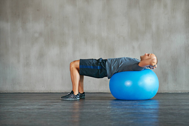 Man, fitness and stretching with exercise ball for workout, training or balance at gym. Active male person lying on round object, equipment or support for warm up, health and wellness on mockup space. - Photo, Image