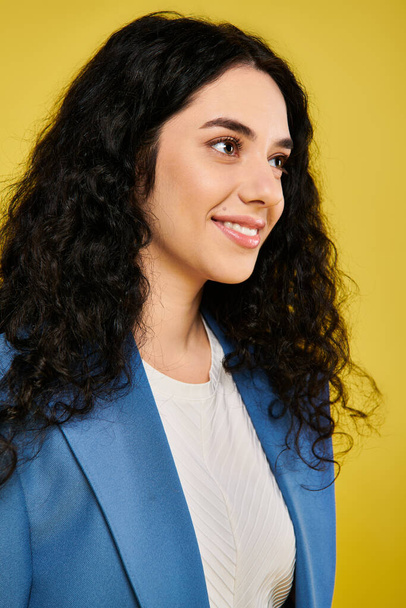 Brünette Frau mit lockigem Haar zeigt ihre Emotionen in einer stylischen blauen Jacke vor gelbem Hintergrund. - Foto, Bild