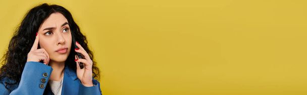 Una joven elegante con el pelo moreno rizado sostiene su mano hasta la oreja, como si estuviera escuchando atentamente, sobre un vibrante fondo amarillo. - Foto, imagen