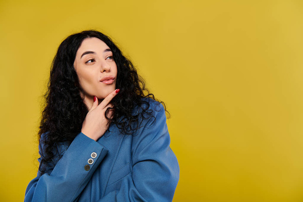 Una giovane donna dai capelli ricci con una giacca blu trasuda eleganza ed emozione mentre posa in uno studio con uno sfondo giallo. - Foto, immagini