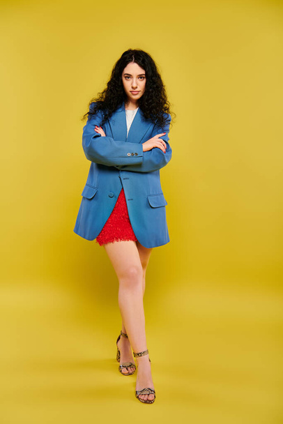 Una giovane bruna dai capelli ricci trasuda fiducia in una giacca blu e una gonna rossa su uno sfondo giallo vibrante. - Foto, immagini