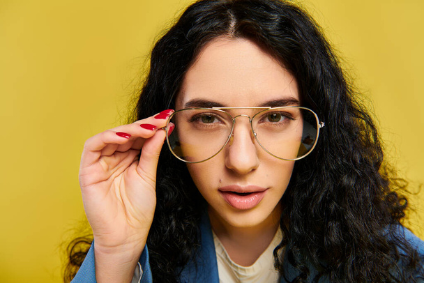 A young woman with long black hair and glasses exudes confidence and intelligence in a stylish setting with a yellow backdrop. - Photo, Image
