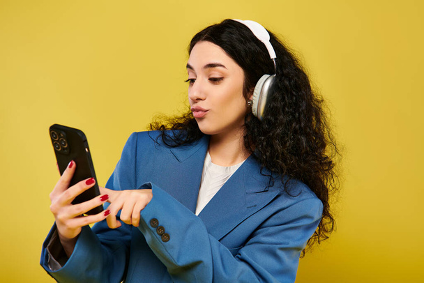 Una giovane donna bruna con le cuffie guarda il suo cellulare, immersa nella musica che suona attraverso le sue orecchie. - Foto, immagini