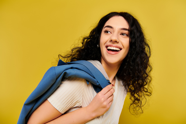 Stylowa młoda kobieta z kręconymi włosami emanuje pewnością siebie, nosząc uderzający niebieski szalik na szyi na żywym żółtym tle. - Zdjęcie, obraz