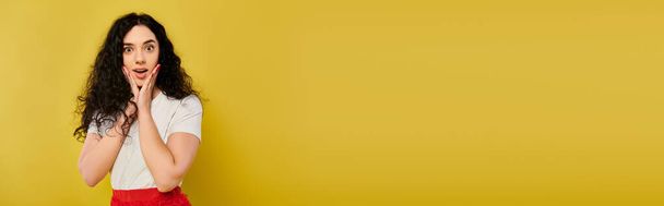 Una joven y elegante morena con el pelo rizado posa emocionalmente delante de una vibrante pared amarilla. - Foto, imagen