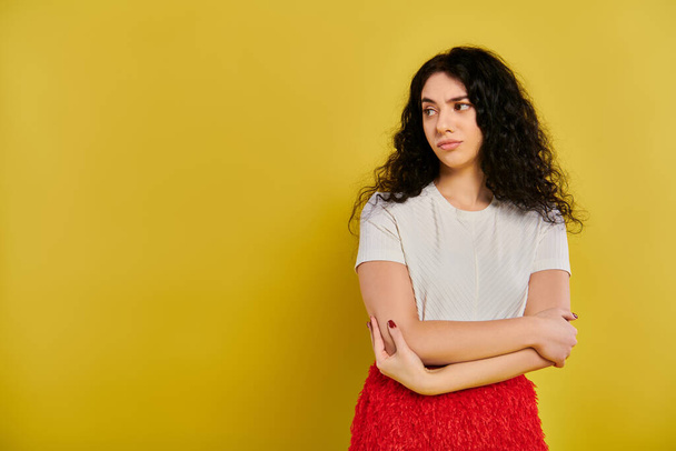 A stylish young woman with curly hair stands confidently with crossed arms against a vibrant yellow backdrop. - Photo, Image