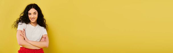 Una giovane donna bruna con i capelli ricci posa in abiti eleganti, esprimendo le sue emozioni di fronte a una vibrante parete gialla. - Foto, immagini
