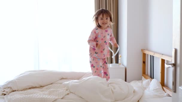 Bebek pijamalarıyla yatakta zıplıyor. Güneşli bir sabah. Mutlu çocuk - Video, Çekim
