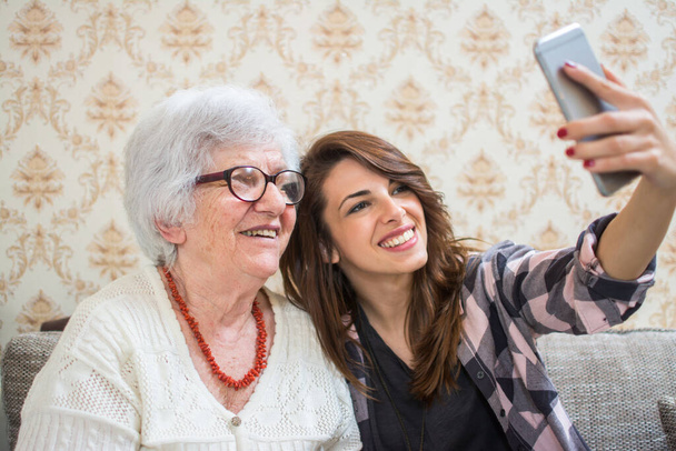 Улыбающиеся бабушка и внучка делают селфи фото на смартфоне
 - Фото, изображение