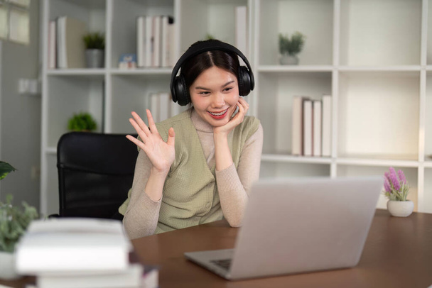 Videokonference. Usmívající se asijská žena s web call na notebooku doma, mluvení na kameru, zatímco sedí na stole v obývacím pokoji doma. - Fotografie, Obrázek