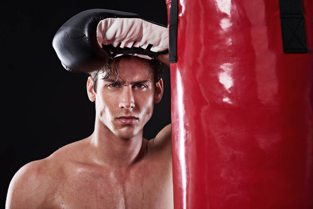 Boxer, pot a portrét muže ve studiu s boxovací taškou pro cvičení, cvičení nebo boj s konkurencí s tmavým pozadím. Box, sport a seriózní sportovec pro trénink, bojová umění nebo fitness. - Fotografie, Obrázek