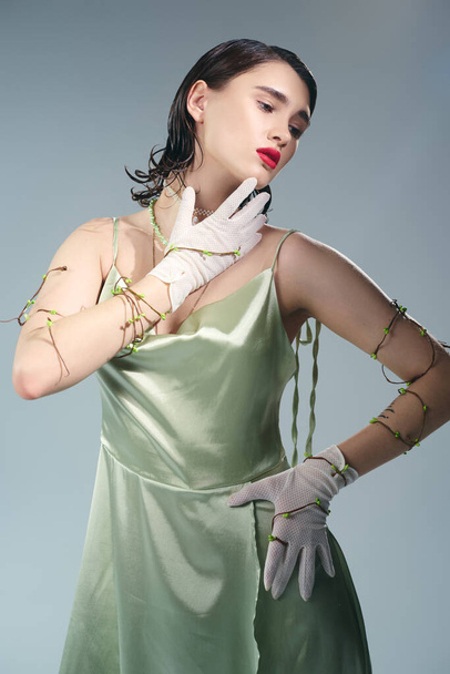 Μια νεαρή όμορφη γυναίκα με κόκκινα χείλη ποζάροντας με πράσινο φόρεμα και λευκά γάντια σε ένα σκηνικό στούντιο σε γκρι φόντο. - Φωτογραφία, εικόνα