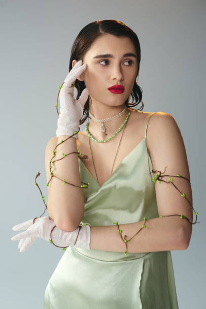 A young, beautiful woman with red lips poses gracefully in a green dress and white gloves in a studio setting on a grey background. - Photo, Image