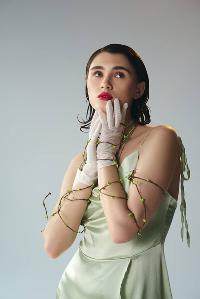 A beautiful young woman with red lips striking a pose in a green dress and white gloves in a studio setting on a grey background. - Photo, Image