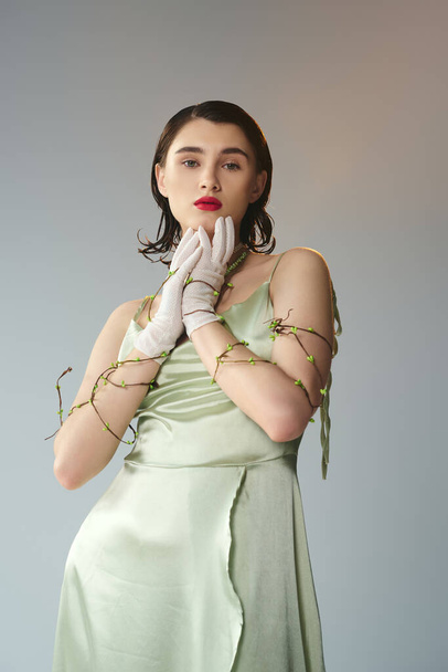 Une jeune belle femme aux lèvres rouges posant en robe verte et gants blancs dans un décor de studio mystique sur fond gris. - Photo, image