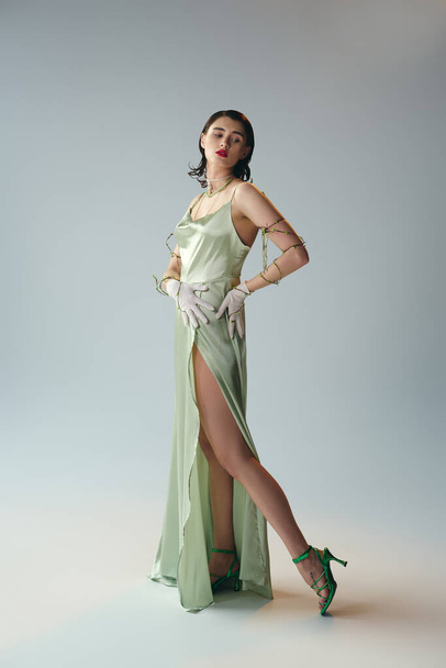 A young woman with red lips striking a pose in a stunning green dress and gloves in a studio setting on a grey background. - Photo, Image