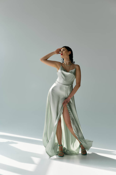 Eine junge, schöne Frau posiert in einem fließenden Kleid und eleganten Handschuhen in einem Studio vor grauem Hintergrund. - Foto, Bild