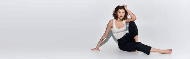 Une jeune femme en pantalon noir et débardeur blanc exécute gracieusement une pose de yoga dans un studio - Photo, image