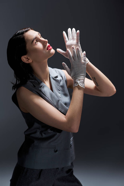 Una giovane donna elegante in un abito elegante con un gilet alzando le mani in aria in un ambiente studio su uno sfondo grigio. - Foto, immagini