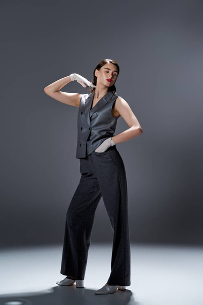 Elegante jovem mulher em elegante colete cinza e calças posa com confiança em um estúdio em um fundo cinza. - Foto, Imagem