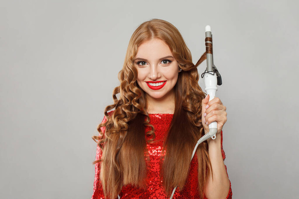 Attractive young glamorous woman with long straight and curly hair holding curling iron on white background. Hair care, hair styling and beauty concept - Photo, Image