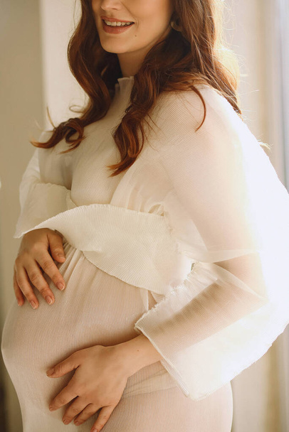 Foto da vicino di donna incinta felice in elegante abito trasparente avorio in studio. Felice maternità - Foto, immagini