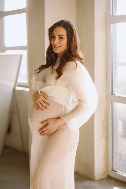 Ritratto di donna bruna incinta in elegante abito avorio in studio. Elegante concetto di gravidanza. Bellezza e moda - Foto, immagini