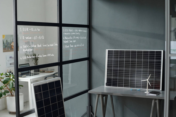 Scrivania grigia con modelli di pannello solare e mulino a vento a muro di spaziosi uffici moderni con postazioni di lavoro di architetti e designer - Foto, immagini