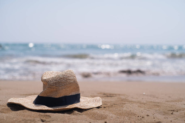 Plajda dinlenen hasır şapka, sahil tatil beldeleri ve çevre dostu turizmi çağrıştırıyor. Kıyı bölgelerinde sükunet ve sürdürülebilirliği keşfet. - Fotoğraf, Görsel
