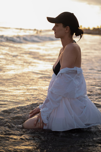 Ein Mädchen sitzt im Morgengrauen am Strand und verkörpert Ruhe und Gelassenheit. Popularisierung von Tourismus, Resorts, gesundem Lebensstil und Outdoor-Sport. - Foto, Bild