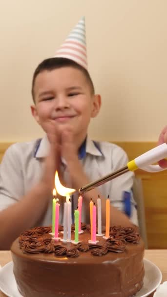 The boy sits in front of a table with a festive cake and candles, blows them out and receives gifts. Birthday celebration concept. vertical video - Footage, Video