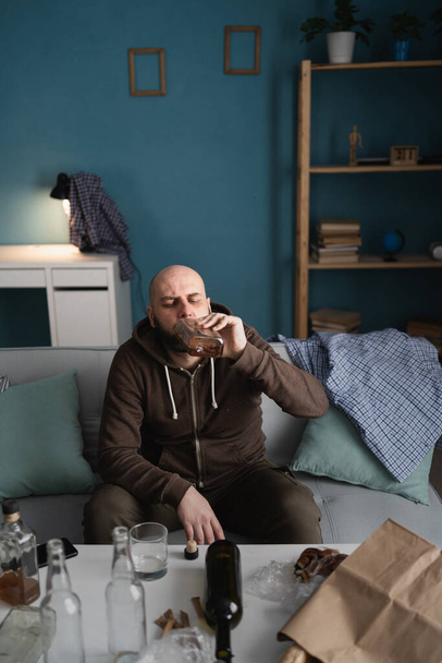 Yksinäinen surullinen masentunut mies juo viskiä kotona istuen sotkuisessa olohuoneessa. Riippuvuuden ja alkoholismin käsite. Kopioi tilaa. Korkea kulma - Valokuva, kuva