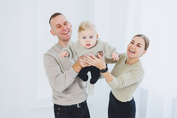 Χαμογελώντας μητέρα και πατέρας κρατώντας ένα παιδί. Γονείς μαμά και ο μπαμπάς και χαμογελαστό μωρό στην αγκαλιά απομονώνονται σε λευκό φόντο. Ευτυχισμένη οικογένεια.. - Φωτογραφία, εικόνα