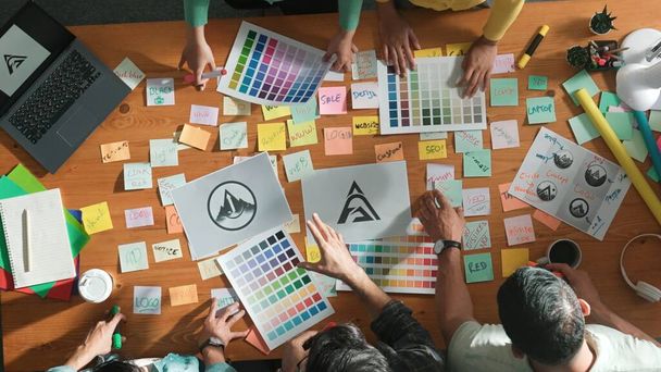 ビジネスチームのトップビューは,アイデアを説明しながら,カラフルな粘着性のあるノートとデザインの会議テーブルにグラフィックロゴを書きます. プロジェクトマネージャーがアイデアを共有し,コンセプトアートをスマートチームに説明します. シンポジウム. - 写真・画像