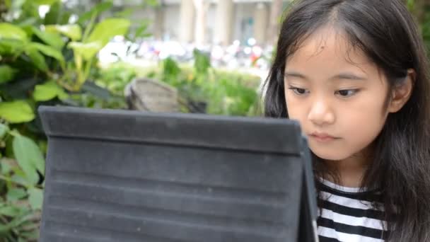 kleine asiatische Mädchen spielen Tablet auf dem Tisch - Filmmaterial, Video