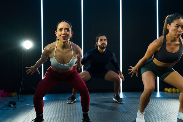 Istruttore entusiasta conduce una classe di fitness ad alta energia con partecipanti concentrati che eseguono squat - Foto, immagini