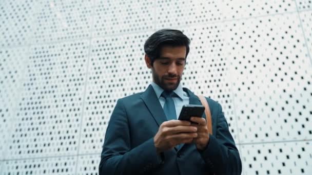 Professional manager looking at mobile phone with white background. Businessman checking phone while reading email by using phone while standing in front of white building. Moving camera. Exultant. - Footage, Video