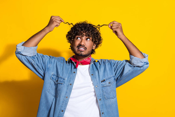Photo portrait of handsome young guy look worried curly strands dressed stylish jeans garment red scarf isolated on yellow color background. - Φωτογραφία, εικόνα